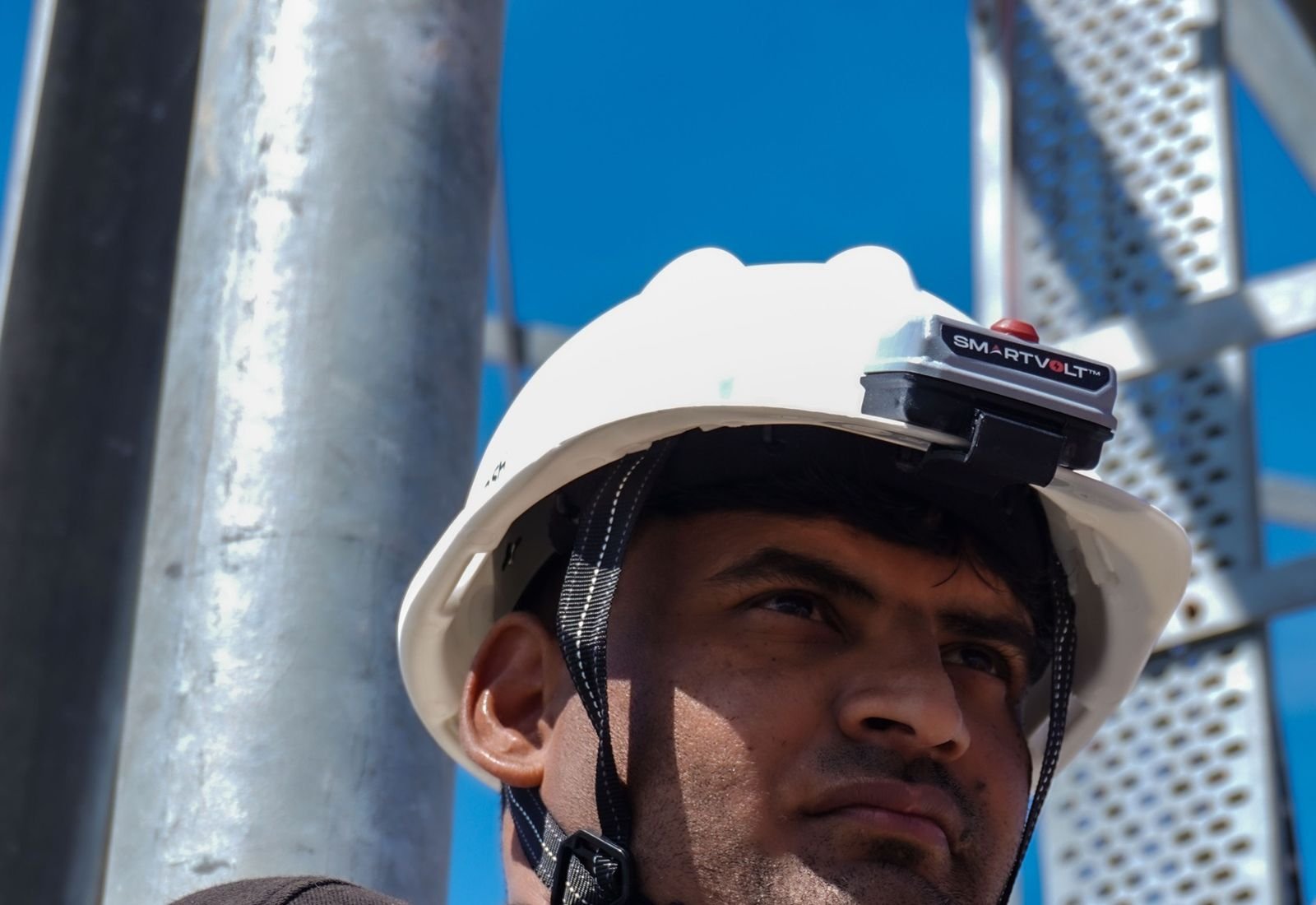 Lineman at a steel tower wearing a SmartVolt voltage detector on the front of his white safety helmet